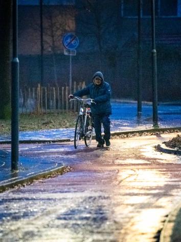 Een man loopt met zijn fiets aan de hand over een glad fietspad heen 