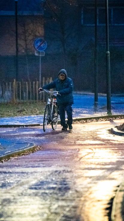 Een man loopt met zijn fiets aan de hand over een glad fietspad heen 