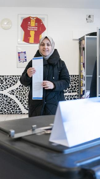 Vrouw met hoofddoek loopt van stemhokje met opgevouwen stembiljet