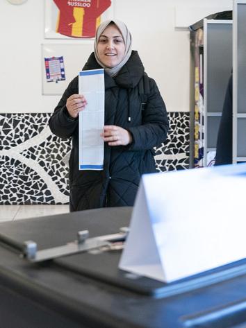 Vrouw met hoofddoek loopt van stemhokje met opgevouwen stembiljet
