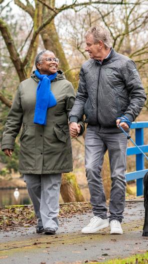 een koppel wandelt hand in hand met de hond door een parkje