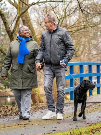 een koppel wandelt hand in hand met de hond door een parkje