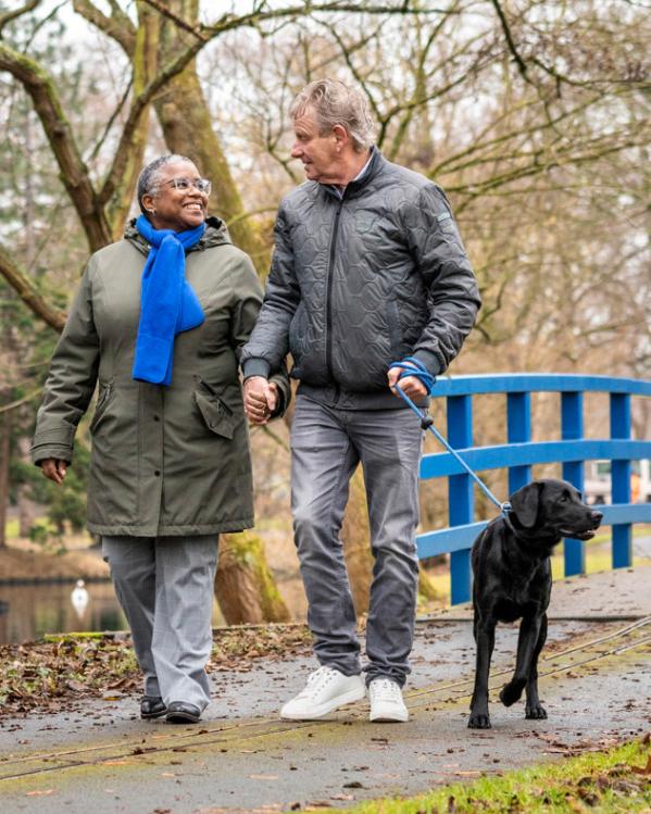 een koppel wandelt hand in hand met de hond door een parkje