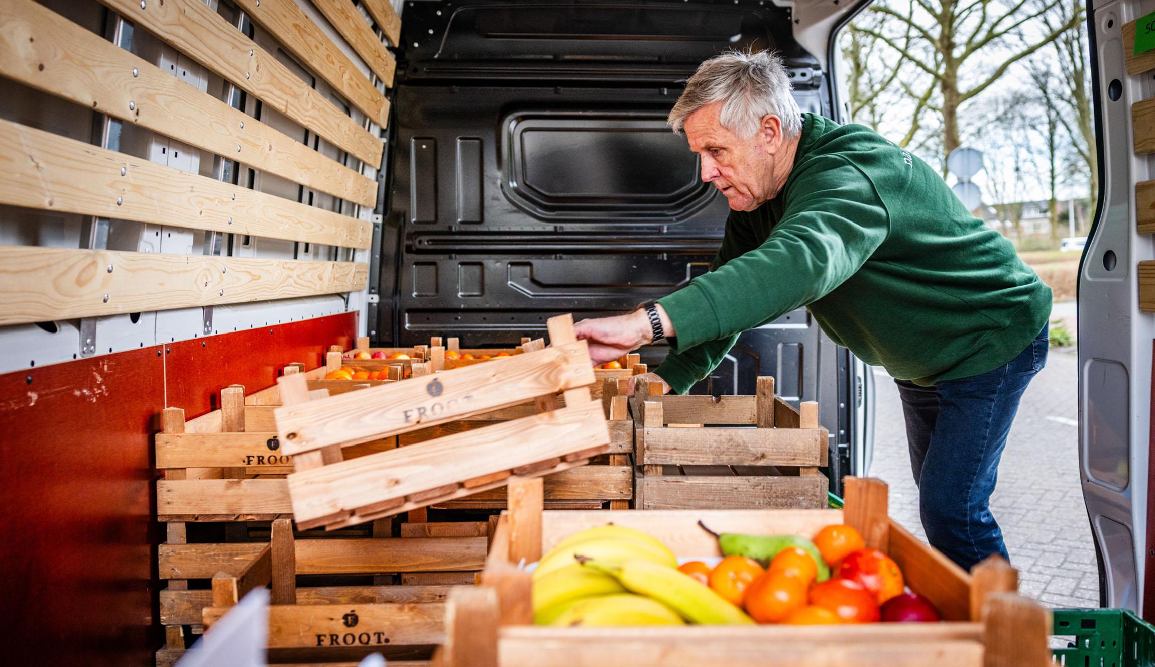 een man met grijze haren aan het werk, hij pakt kratten met fruit en groente uit een busje