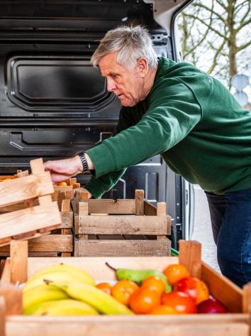 een man met grijze haren aan het werk, hij pakt kratten met fruit en groente uit een busje