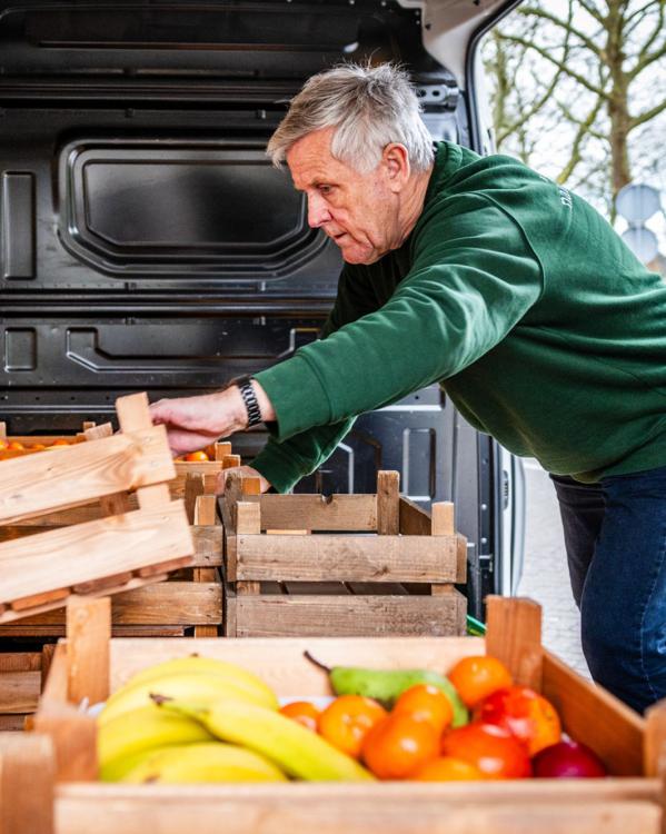 een man met grijze haren aan het werk, hij pakt kratten met fruit en groente uit een busje