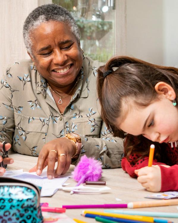 een gepensioneerde vrouw vrolijk lachend naast haar kleindochter terwijl haar kleindochter aan het tekenen is