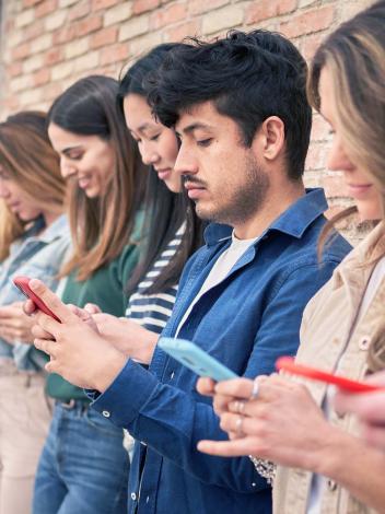 meerdere mensen op een rij die op hun eigen mobiele telefoon kijken