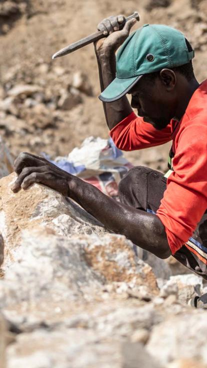 Een mijnwerker hakt op stenen bij een lithiummijn in Nigeria.