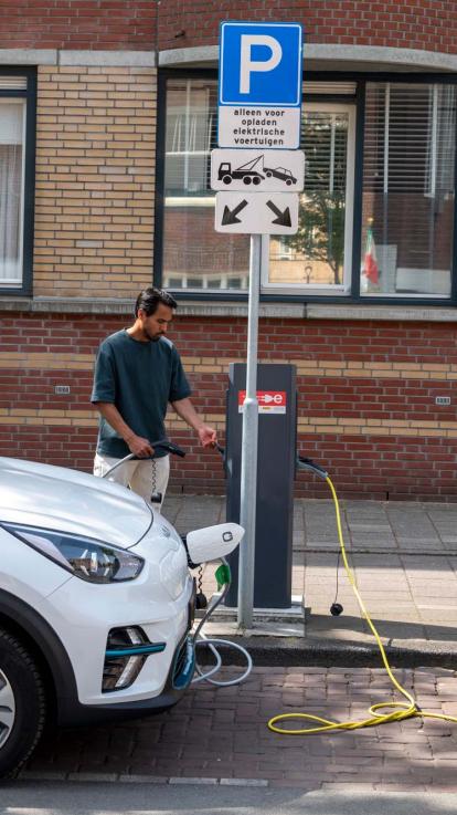 Een man stopt de stekker van zijn elektrische (deel)auto in de laadpaal