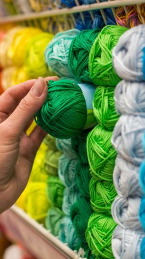 Een hand reikt naar een groen bolletje garen.