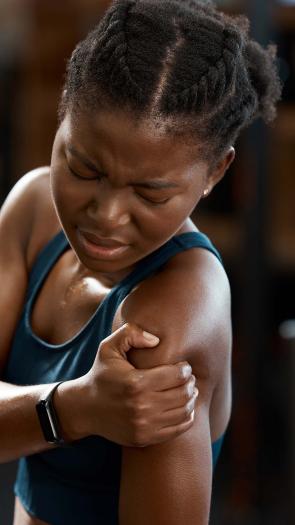 Een jonge vrouw houdt haar schouder vast, het lijkt alsof ze erg pijn heeft.