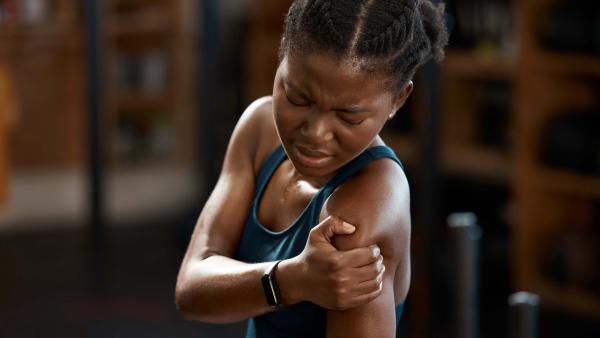 Een jonge vrouw houdt haar schouder vast, het lijkt alsof ze erg pijn heeft.