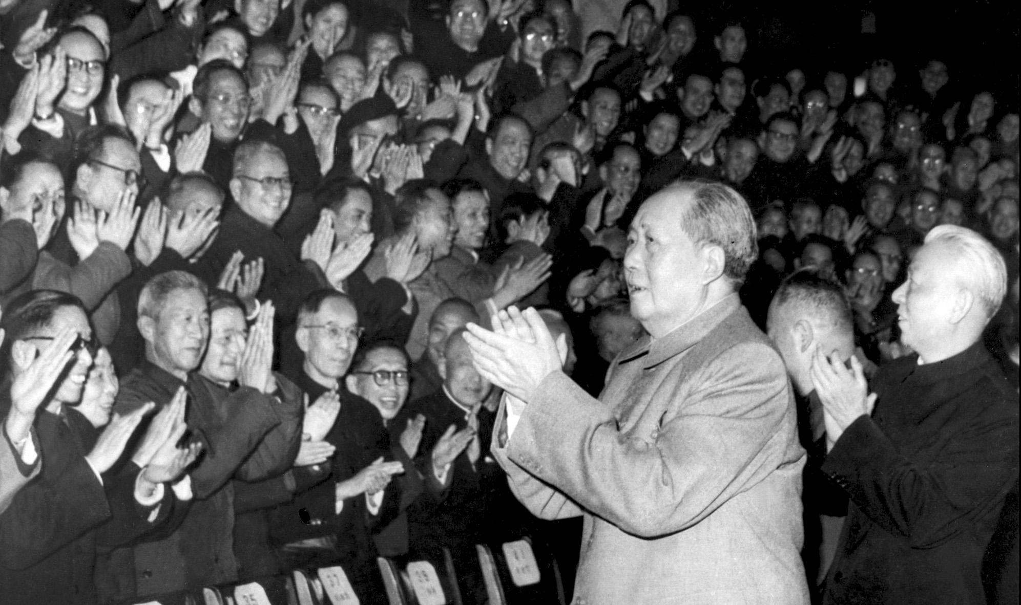 Een zwart-witfoto van een klappende Mao Zedong die wordt gevolgd door Liu Shaoqi. Ze lopen langs een klappend publiek.