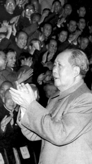 Een zwart-witfoto van een klappende Mao Zedong die wordt gevolgd door Liu Shaoqi. Ze lopen langs een klappend publiek.