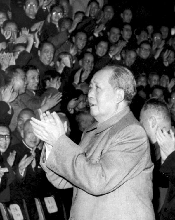 Een zwart-witfoto van een klappende Mao Zedong die wordt gevolgd door Liu Shaoqi. Ze lopen langs een klappend publiek.