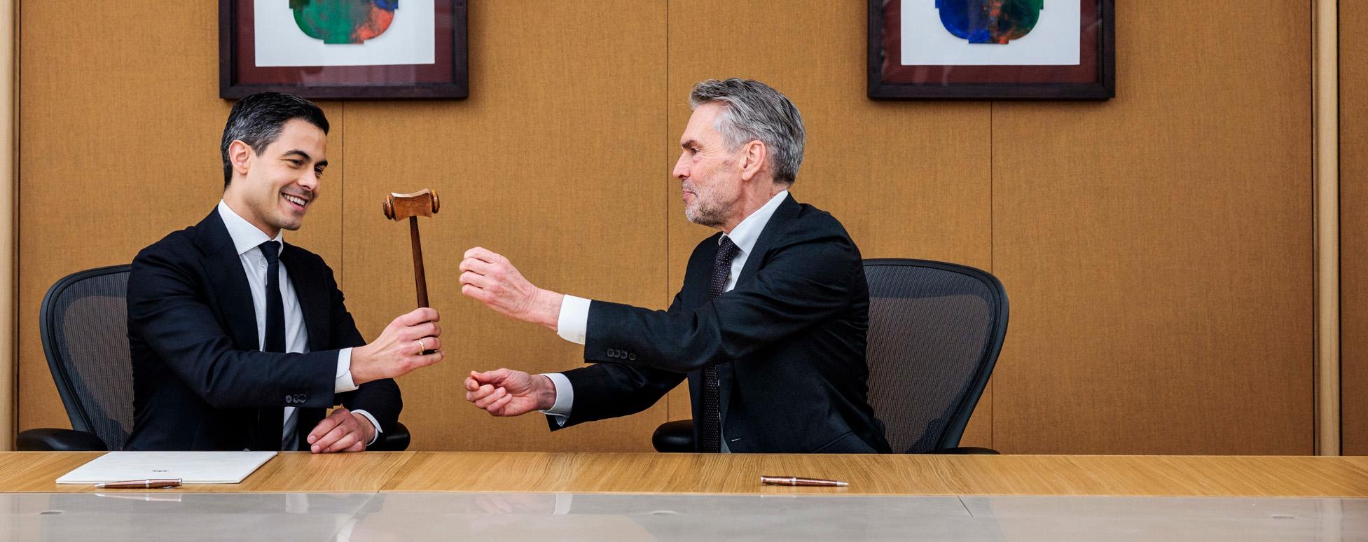 Oud-premier Dick Schoof draagt de symbolische hamer van het premierschap over aan Rob Jetten. Ze zitten samen aan een tafel.