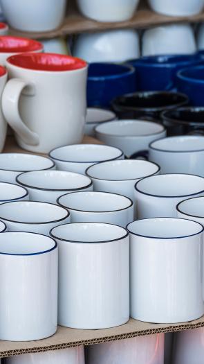 Verschillende soorten koffiebekers, wit, rood, blauw, zwart, in verschillende vormen staan opgestapeld.