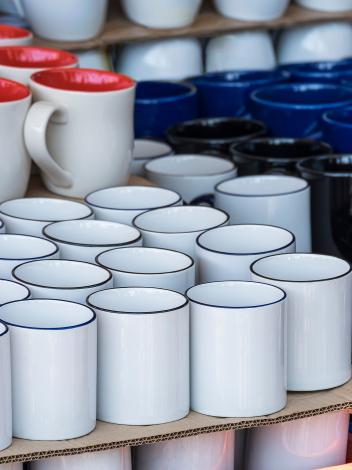 Verschillende soorten koffiebekers, wit, rood, blauw, zwart, in verschillende vormen staan opgestapeld.