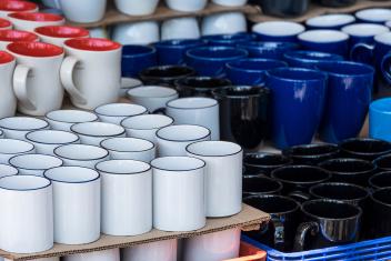 Verschillende soorten koffiebekers, wit, rood, blauw, zwart, in verschillende vormen staan opgestapeld.
