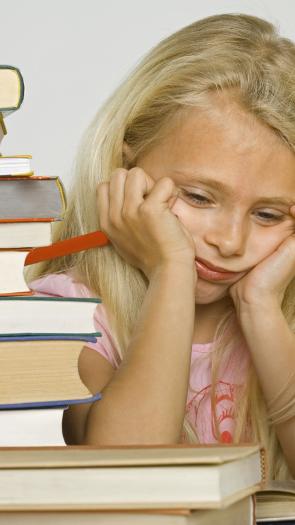 Een jong meisje zit omringd door boeken, ze kijkt verdrietig.