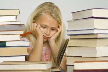 Een jong meisje zit omringd door boeken, ze kijkt verdrietig.