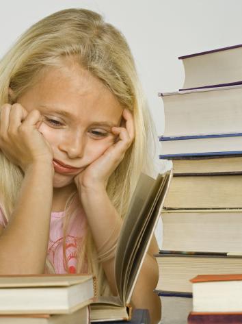 Een jong meisje zit omringd door boeken, ze kijkt verdrietig.