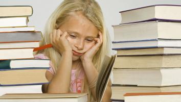 Een jong meisje zit omringd door boeken, ze kijkt verdrietig.