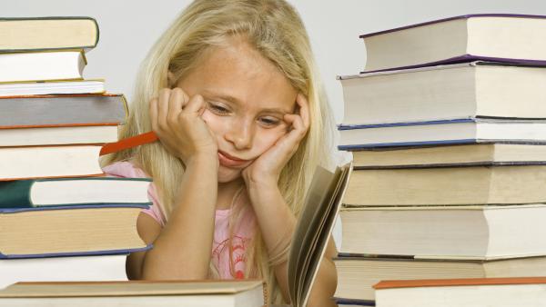 Een jong meisje zit omringd door boeken, ze kijkt verdrietig.