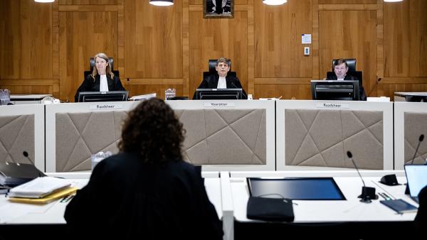 Meervoudige rechtszaal met 3 rechters tegenover een vrouw met krullen