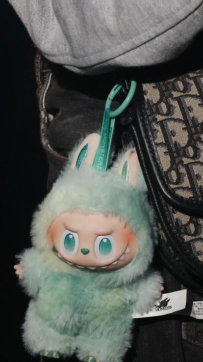 Een turquoise labubu hangt aan een hippe Diortas.