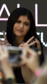 Influencer Kylie Jenner poseert voor fans die haar fotograferen met twee peace tekens in de lucht.