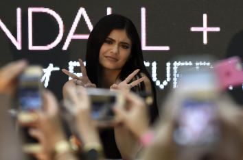 Influencer Kylie Jenner poseert voor fans die haar fotograferen met twee peace tekens in de lucht.