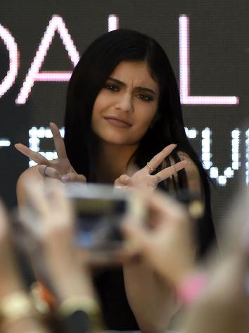 Influencer Kylie Jenner poseert voor fans die haar fotograferen met twee peace tekens in de lucht.