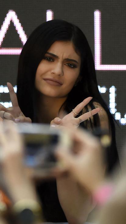 Influencer Kylie Jenner poseert voor fans die haar fotograferen met twee peace tekens in de lucht.