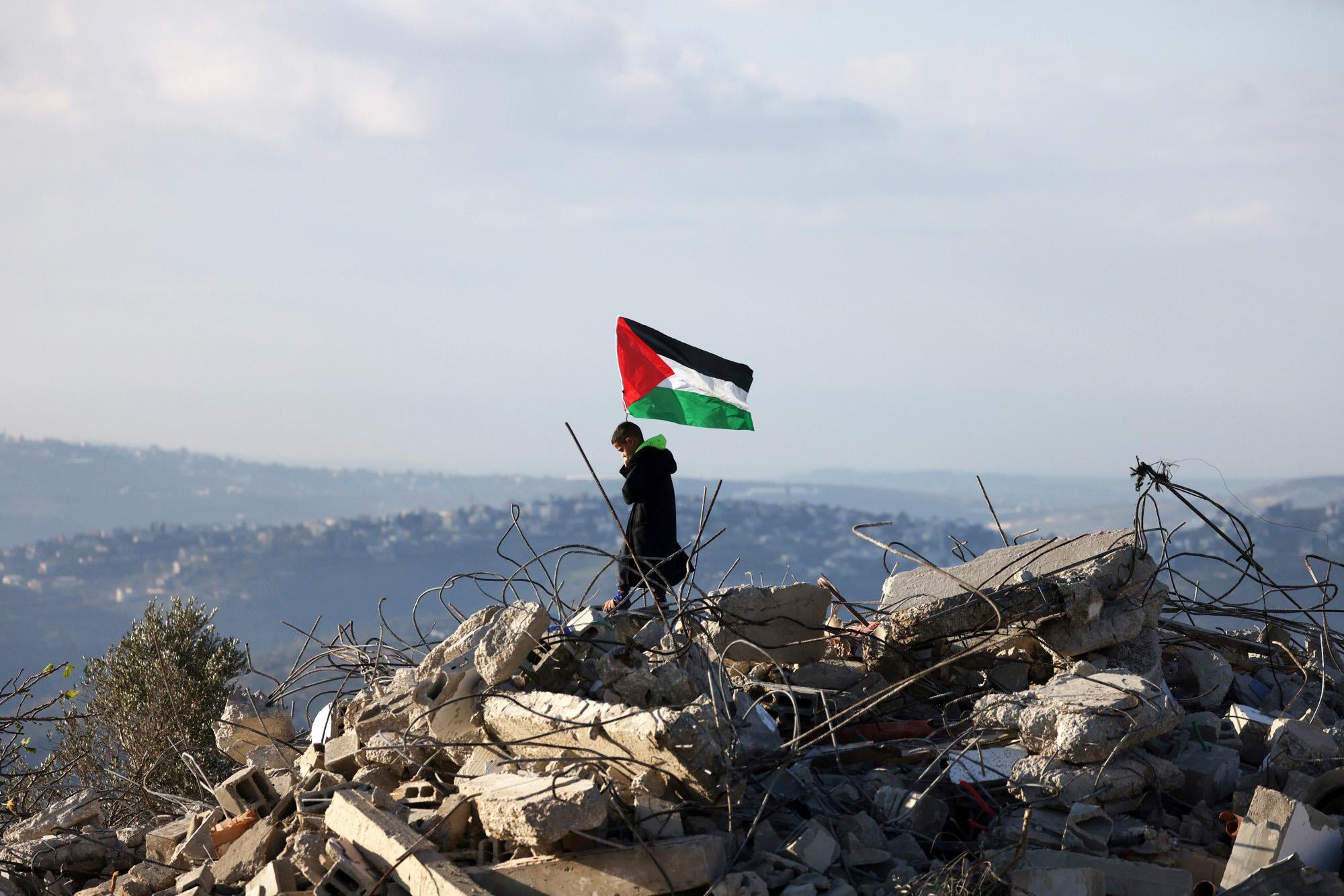 Een Palestijns kind staat met een Palestijnse vlag bovenop de resten van een Palestijns huis dat door Israëlische militairen is vernietigd.