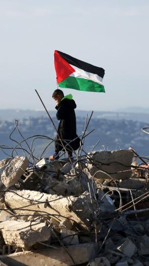 Een Palestijns kind staat met een Palestijnse vlag bovenop de resten van een Palestijns huis dat door Israëlische militairen is vernietigd.