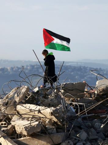 Een Palestijns kind staat met een Palestijnse vlag bovenop de resten van een Palestijns huis dat door Israëlische militairen is vernietigd.