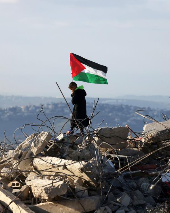 Een Palestijns kind staat met een Palestijnse vlag bovenop de resten van een Palestijns huis dat door Israëlische militairen is vernietigd.