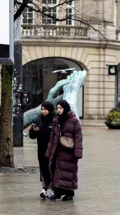 Twee vrouwen met dezelfde outfit lopen in Amsterdam langs een bord voor de gemeenteraadsverkeizingen.