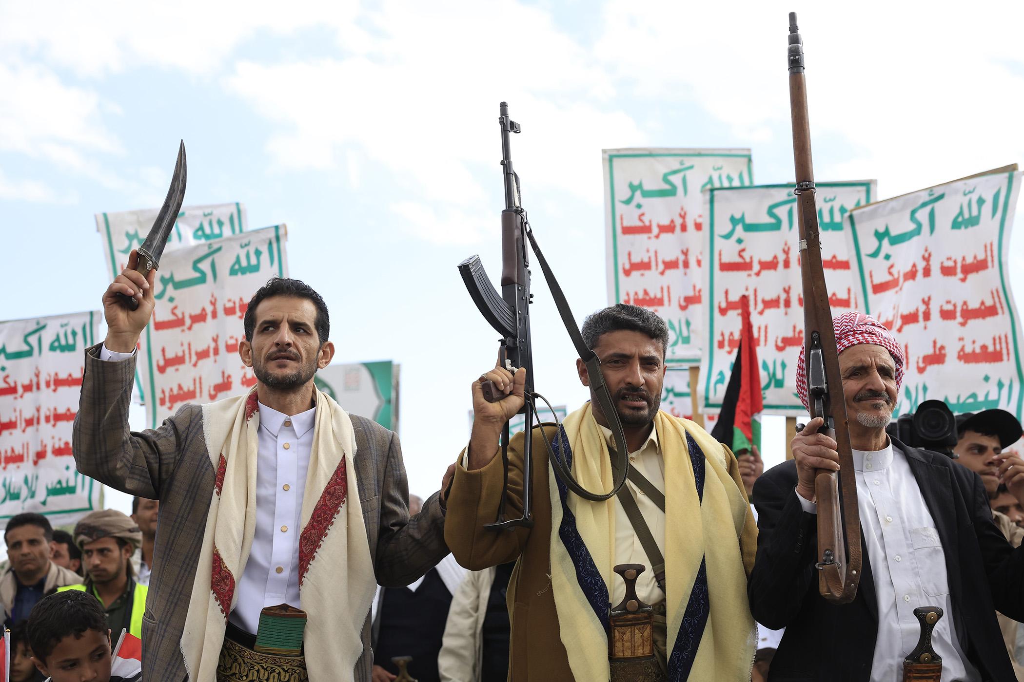 Houthi supporters houden wapens in de lucht. Achter de mannen zijn borden met arabische tekst te zien