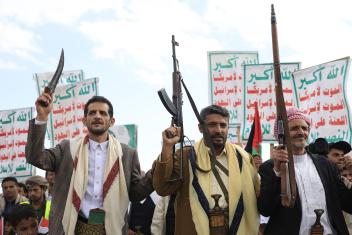 Houthi supporters houden wapens in de lucht. Achter de mannen zijn borden met arabische tekst te zien