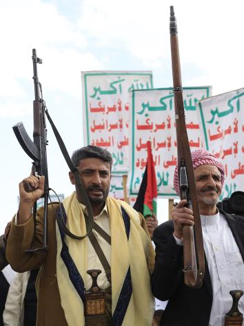 Houthi supporters houden wapens in de lucht. Achter de mannen zijn borden met arabische tekst te zien