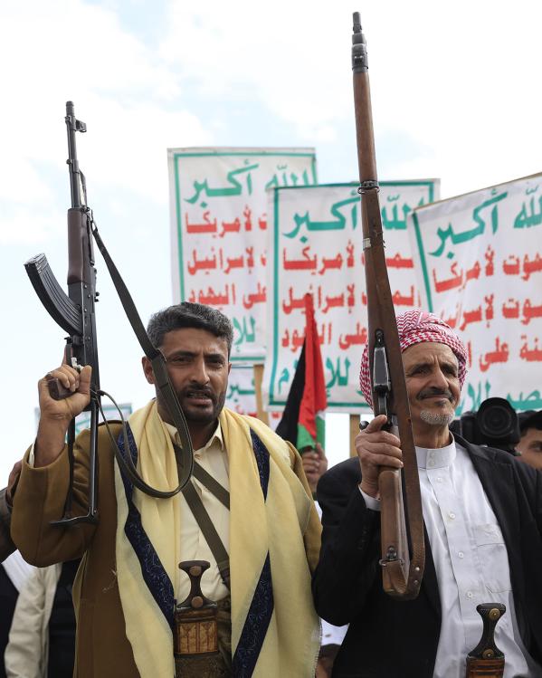 Houthi supporters houden wapens in de lucht. Achter de mannen zijn borden met arabische tekst te zien