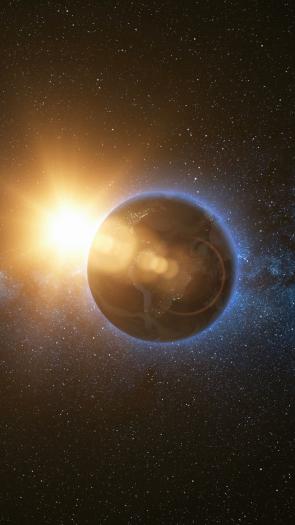 Een foto van de aarde waarachter het licht van de zon doorkomt.