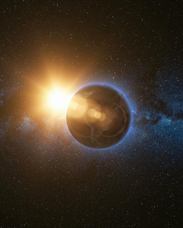 Een foto van de aarde waarachter het licht van de zon doorkomt.