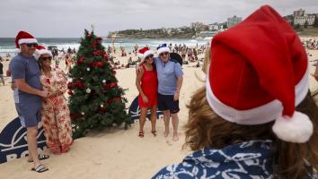 toeristen met kerstmutsen poseren bij een kerstboom op het strand
