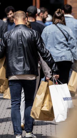 Een man loop in een winkelstraat. Vanaf de achterkant zien we dat hij veel verschillende winkeltassen vast heeft.