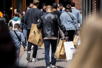 Een man loop in een winkelstraat. Vanaf de achterkant zien we dat hij veel verschillende winkeltassen vast heeft.