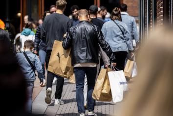 Een man loop in een winkelstraat. Vanaf de achterkant zien we dat hij veel verschillende winkeltassen vast heeft.